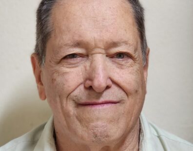 Prof. Dr. Adalberto Bono Maurizio Sacchi Bassi - foto de busto. Senhor de pele clara, idoso, com olhos verdes, cabelo curto e acinzentado e grisalho com roso levemente alongado, vestindo uma camisa com gola verde posando em um fundo bege.